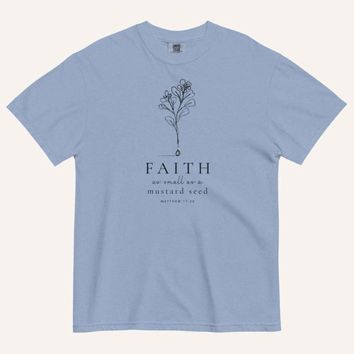 A muted blue short-sleeve crewneck t-shirt with a black line-art mustard seed graphic and the text 'FAITH as small as a mustard seed' and 'MATTHEW 17:20' printed on the front, displayed against a light cream background.