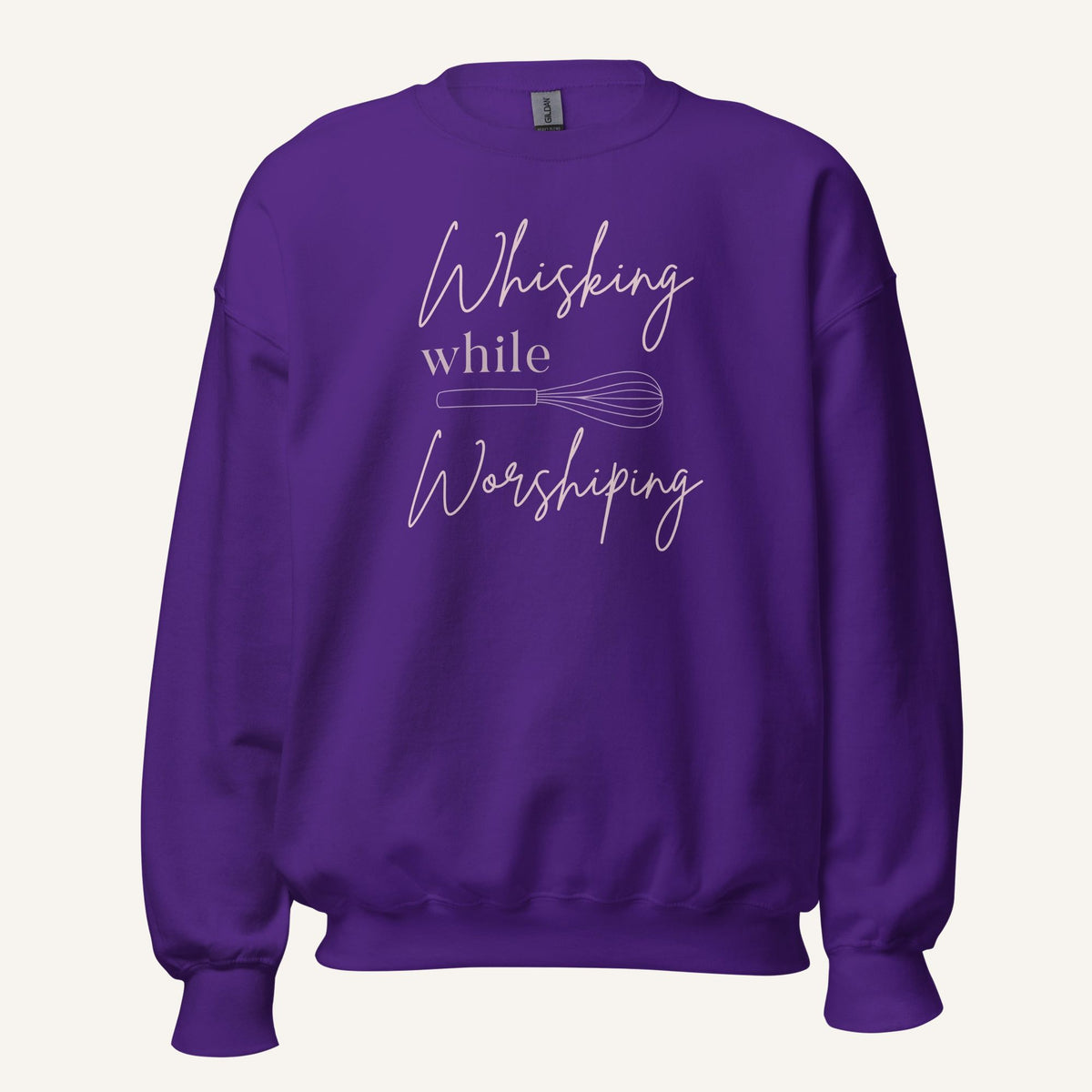 Purple crewneck sweatshirt with "Whisking while Worshiping" pink text with a pink whisk graphic.