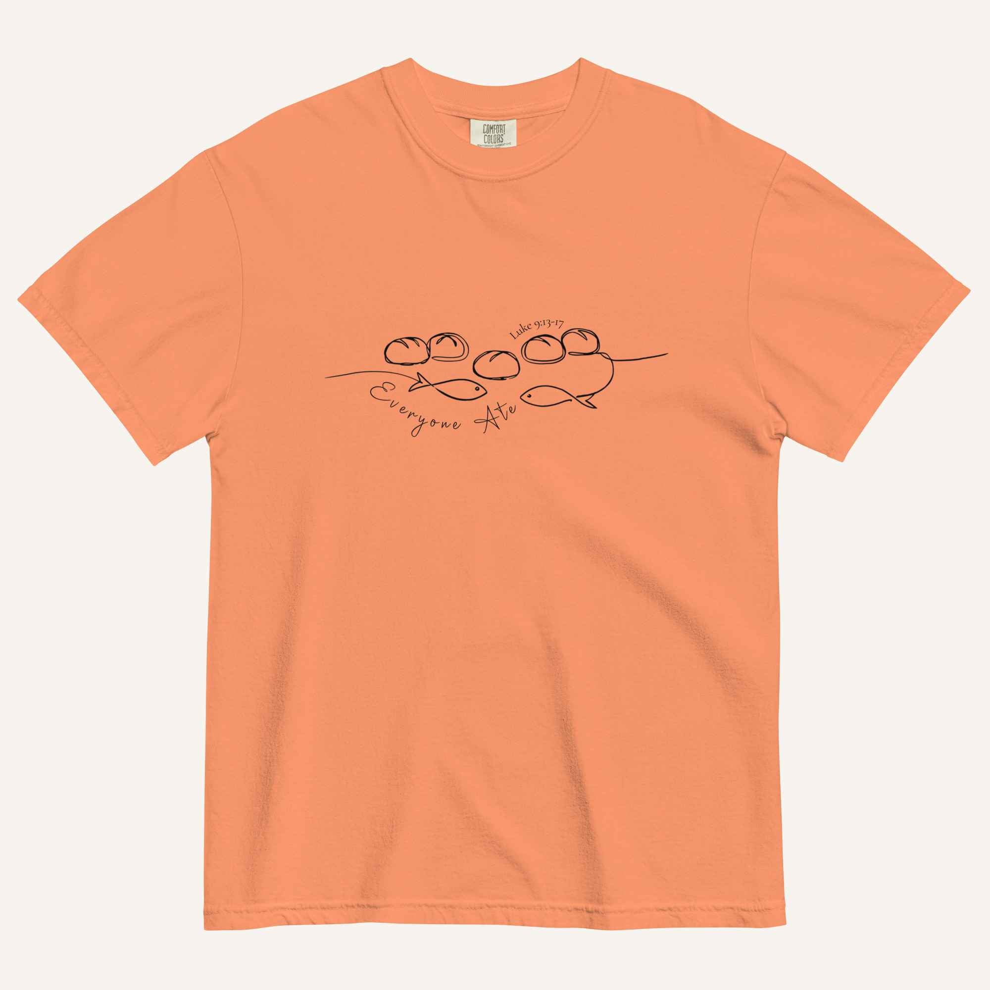 A light pastel orange short-sleeve crewneck t-shirt with a black graphic of two fish and 5 loaves of bread on a line and the cursive text 'Everyone Ate' across the chest, displayed flat against a light beige background.