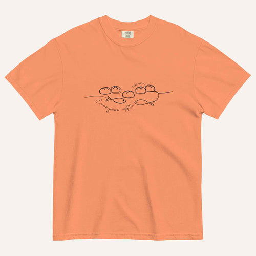A light pastel orange short-sleeve crewneck t-shirt with a black graphic of two fish and 5 loaves of bread on a line and the cursive text 'Everyone Ate' across the chest, displayed flat against a light beige background.