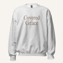 light grey sweatshirt with 'Covered in Grace' text on a cream background