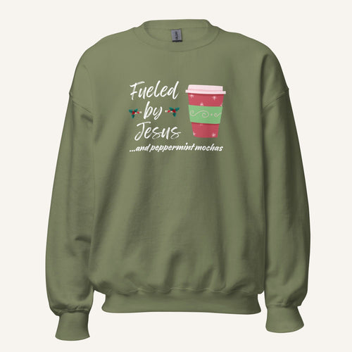 Olive green unisex crewneck sweatshirt featuring a Christmas design with the phrase “Fueled by Jesus …and peppermint mochas,” peppermint illustrations, and a festive red and green peppermint mocha cup graphic.