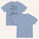 A muted dusty blue t-shirt shown from both the front and back. The front features a small black cross on the top left. The back features the black text 'There is HOPE in Jesus' in a mix of script and block lettering.