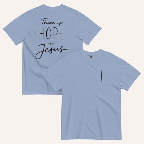 A muted dusty blue t-shirt shown from both the front and back. The front features a small black cross on the top left. The back features the black text 'There is HOPE in Jesus' in a mix of script and block lettering.