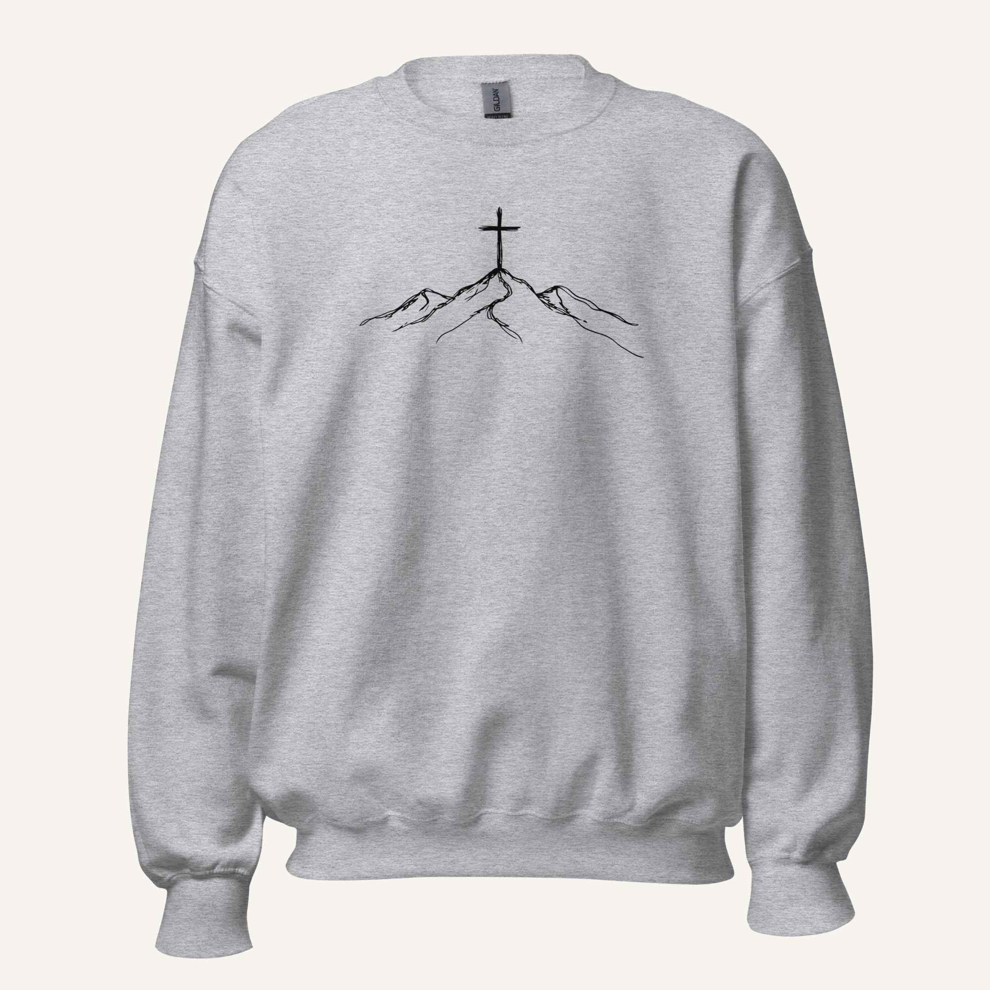 A light heather gray crewneck sweatshirt featuring a black line art graphic of a cross on top of simple mountains on the chest, displayed against a solid off-white background.