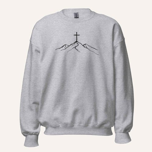 A light heather gray crewneck sweatshirt featuring a black line art graphic of a cross on top of simple mountains on the chest, displayed against a solid off-white background.