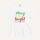 a white t-shirt that has "Merry & Bright" colored text with Christmas lights and star graphics