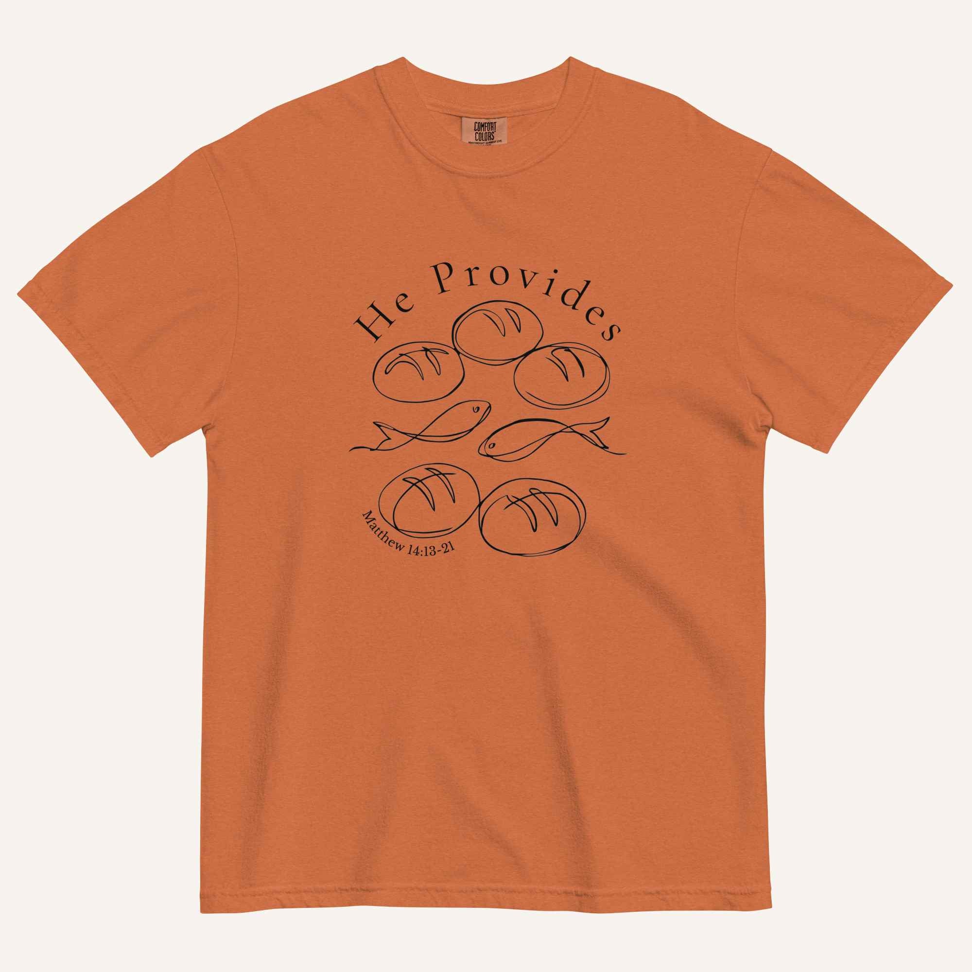 A burnt orange short-sleeve t-shirt with a black graphic print on the front showing fish and loaves of bread, with the text 'He Provides' and 'Matthew 14:13-21'.