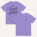 A purple short-sleeve t-shirt shown from both the front and back on a light cream background. The back features the phrase 'God is good all the time' in black script, and the front has a small black cross on the left chest.