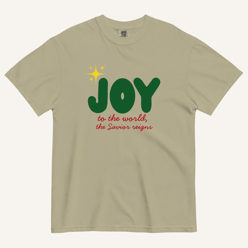 a khaki color t-shirt with the words "Joy to the world, the Savior reigns" in bold colorful font with a star graphic