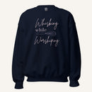Navy crewneck sweatshirt with "Whisking while Worshiping" pink text with a pink whisk graphic.