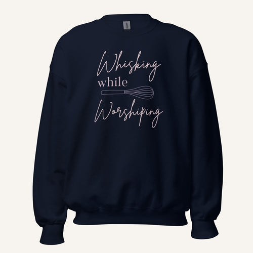 Navy crewneck sweatshirt with "Whisking while Worshiping" pink text with a pink whisk graphic.
