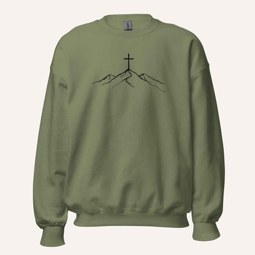 A military green crewneck sweatshirt featuring a black line art graphic of a cross on top of simple mountains on the chest, displayed against a solid off-white background.