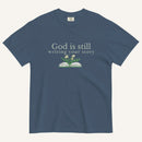 blue t-shirt with 'God is still writing your story' text and book graphic on a white background