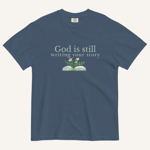 blue t-shirt with 'God is still writing your story' text and book graphic on a white background