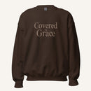 brown sweatshirt with 'Covered in Grace' text on a cream background
