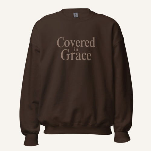 brown sweatshirt with 'Covered in Grace' text on a cream background