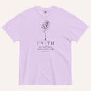 A light purple short-sleeve crewneck t-shirt with a black line-art mustard seed graphic and the text 'FAITH as small as a mustard seed' and 'MATTHEW 17:20' printed on the front, displayed against a light cream background.