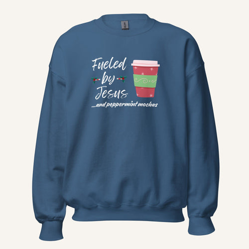 Blue unisex crewneck sweatshirt featuring a Christmas design with the phrase “Fueled by Jesus …and peppermint mochas,” peppermint illustrations, and a festive red and green peppermint mocha cup graphic.