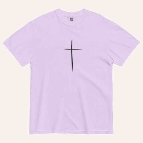 A short-sleeve crewneck t-shirt in a light lavender color, featuring a simple black Christian cross printed on the center chest. The t-shirt is laid flat against a solid, warm off-white background.