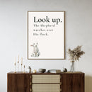 wall art featuring a watercolor lamb looking up with 'Look Up. The Shepherd watches over His flock' text in a neutral living room.