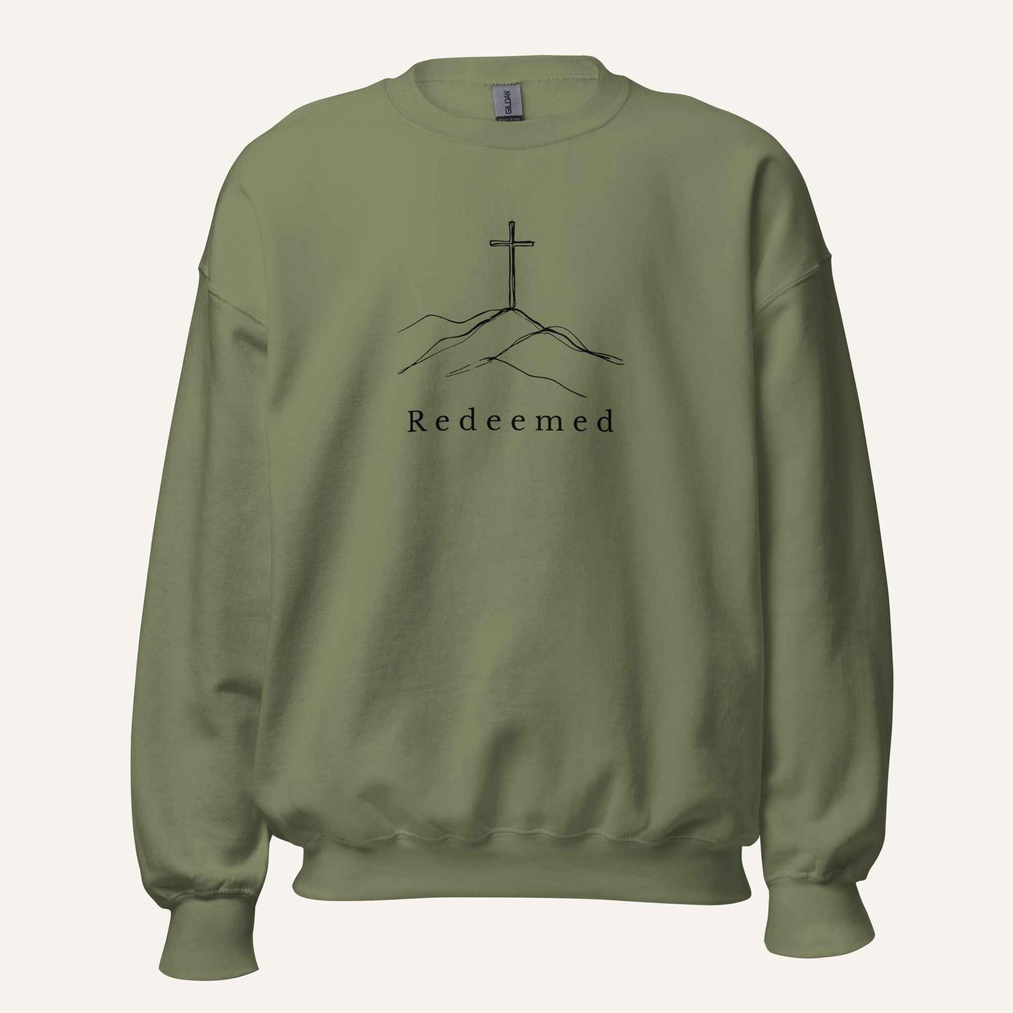 A military green crewneck sweatshirt featuring a black graphic of a cross on a hill with the word 'Redeemed' printed below it, displayed on a clean off-white background.