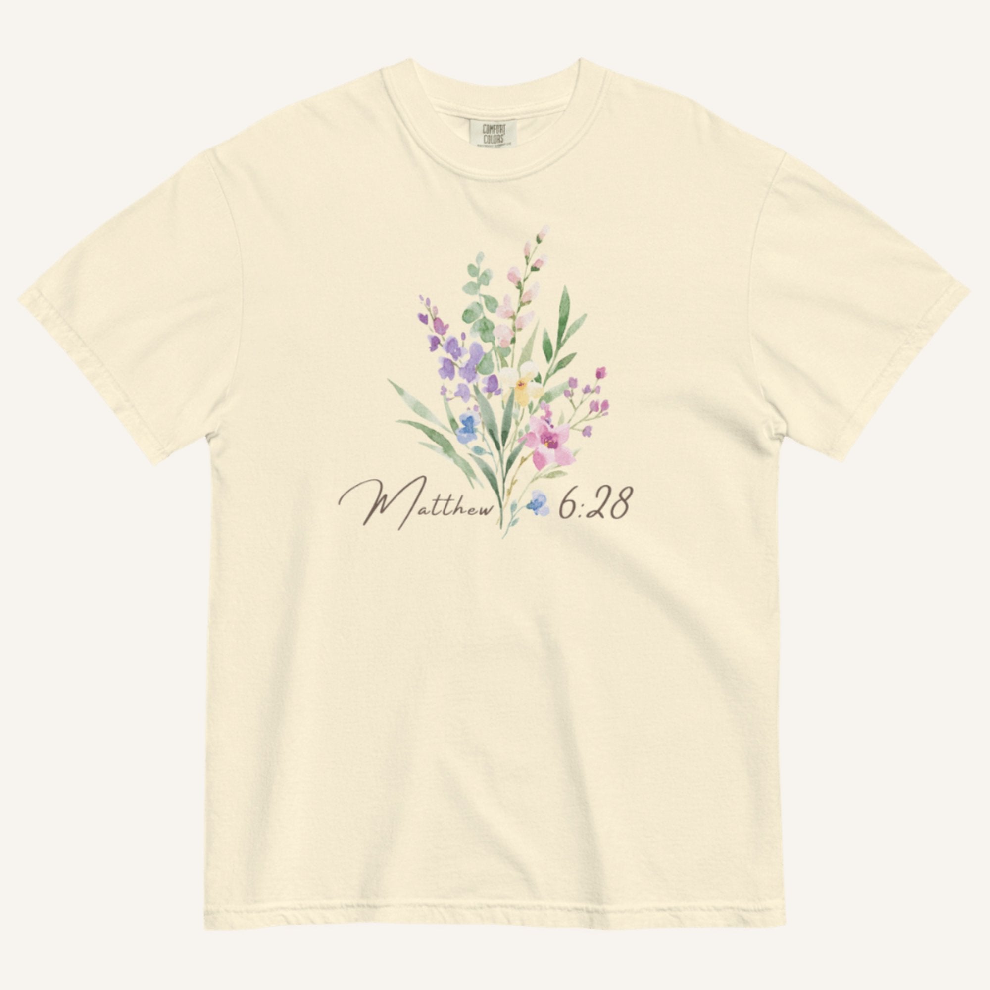 Beige t-shirt with floral design and 'Matthew 6:28' text on a white background