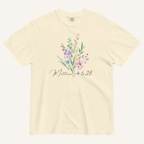 Beige t-shirt with floral design and 'Matthew 6:28' text on a white background