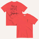 A reddish pink t-shirt shown from both the front and back. The front features a small black cross on the top left. The back features the black text 'There is HOPE in Jesus' in a mix of script and block lettering.