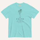 A light blue short-sleeve crewneck t-shirt with a black line-art mustard seed graphic and the text 'FAITH as small as a mustard seed' and 'MATTHEW 17:20' printed on the front, displayed against a light cream background.