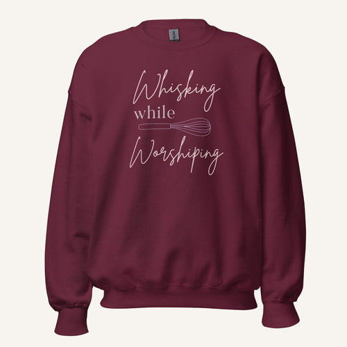 Maroon crewneck sweatshirt with "Whisking while Worshiping" pink text with a pink whisk graphic.