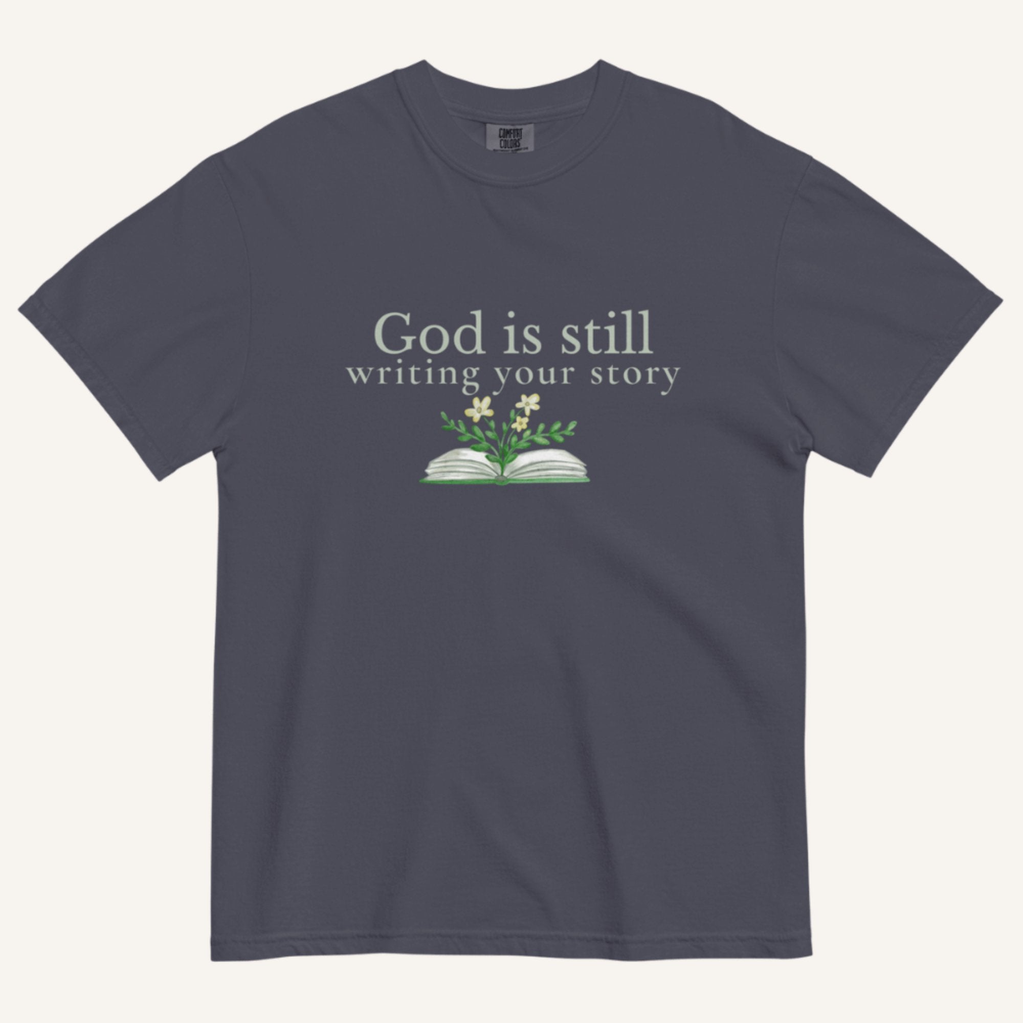 blue grey t-shirt with 'God is still writing your story' text and book graphic on a white background