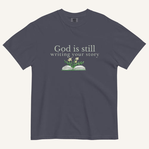 blue grey t-shirt with 'God is still writing your story' text and book graphic on a white background