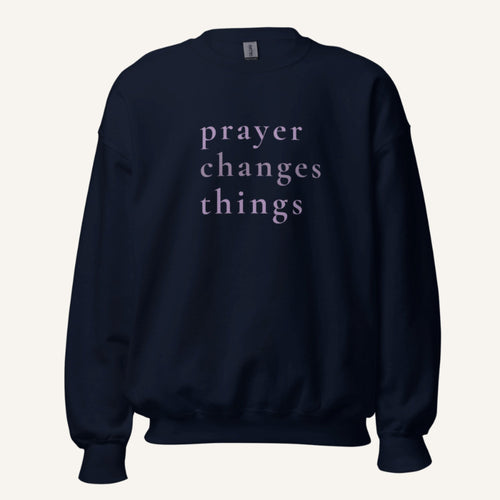 dark navy sweatshirt with 'Prayer Changes Things' purple text on a cream background