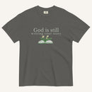 Dark gray t-shirt with 'God is still writing your story' text and book graphic on a white background