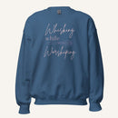 Blue crewneck sweatshirt with "Whisking while Worshiping" pink text with a pink whisk graphic.