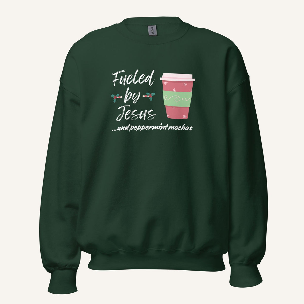 Green unisex crewneck sweatshirt featuring a Christmas design with the phrase “Fueled by Jesus …and peppermint mochas,” peppermint illustrations, and a festive red and green peppermint mocha cup graphic.