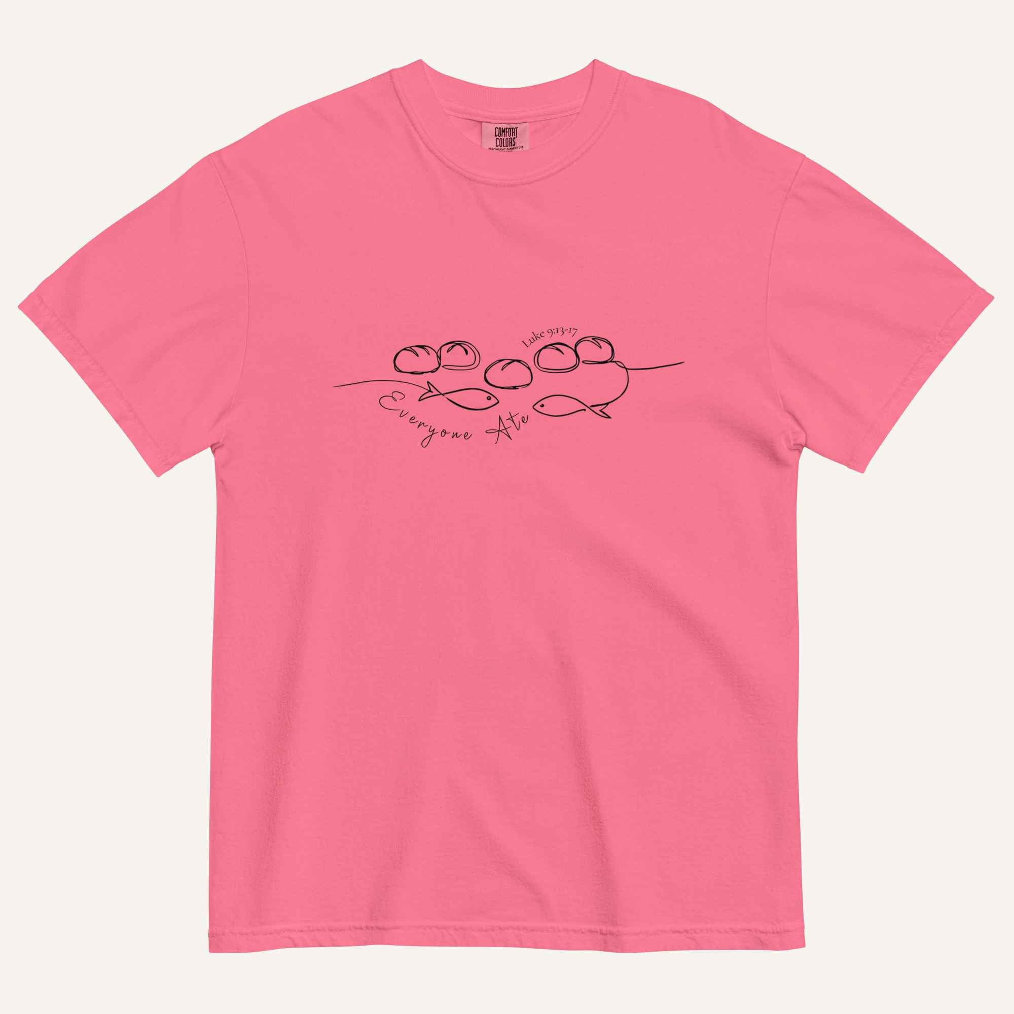 A hot pink short-sleeve crewneck t-shirt with a black graphic of two fish and 5 loaves of bread on a line and the cursive text 'Everyone Ate' across the chest, displayed flat against a light beige background.