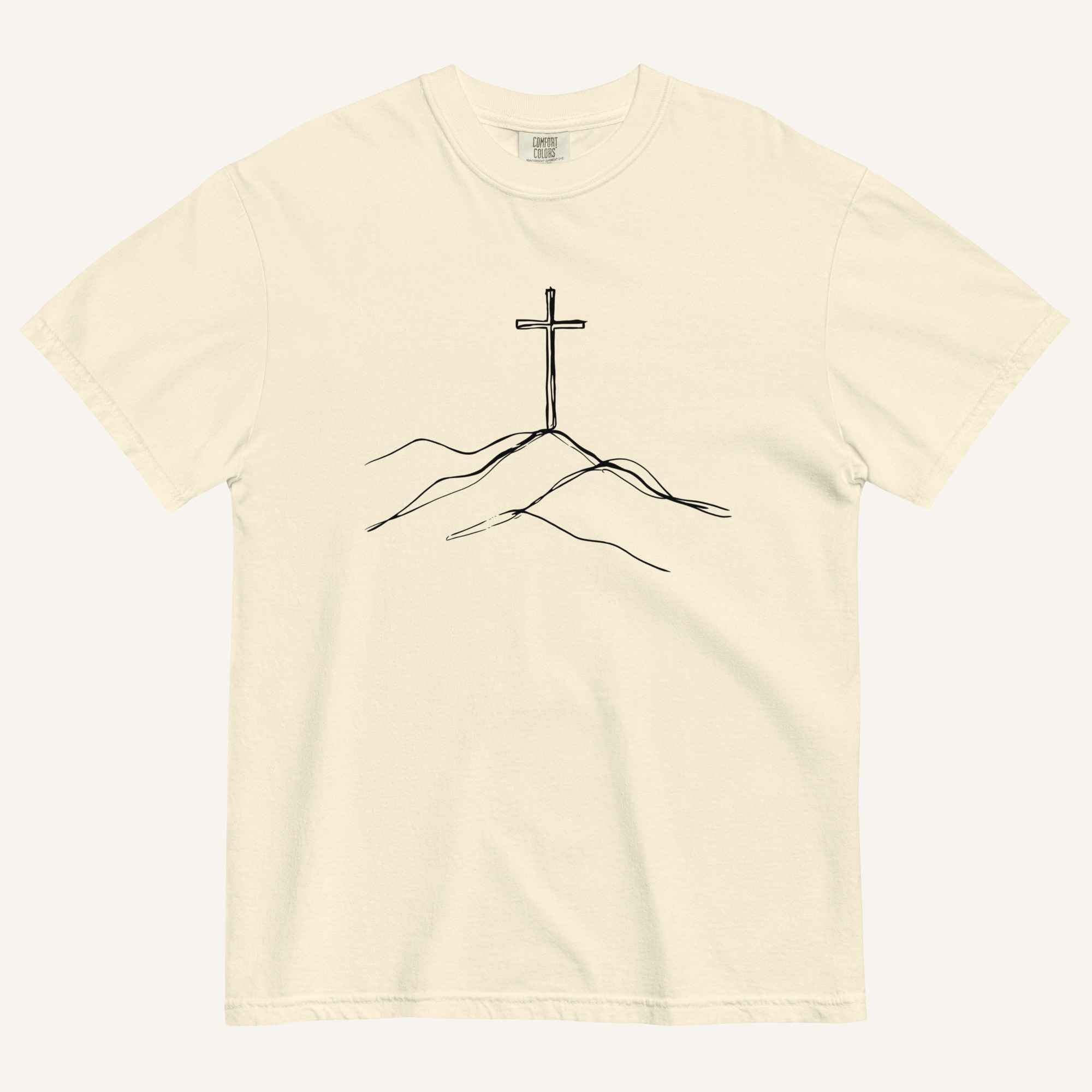 An off-white crewneck t-shirt featuring a minimalist black line art graphic of a cross on a hill, displayed flat against a matching off-white background.