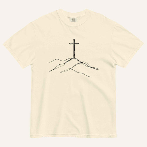 An off-white crewneck t-shirt featuring a minimalist black line art graphic of a cross on a hill, displayed flat against a matching off-white background.