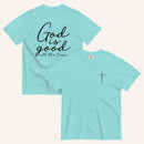 A lagoon blue short-sleeve t-shirt shown from both the front and back on a light cream background. The back features the phrase 'God is good all the time' in black script, and the front has a small black cross on the left chest.
