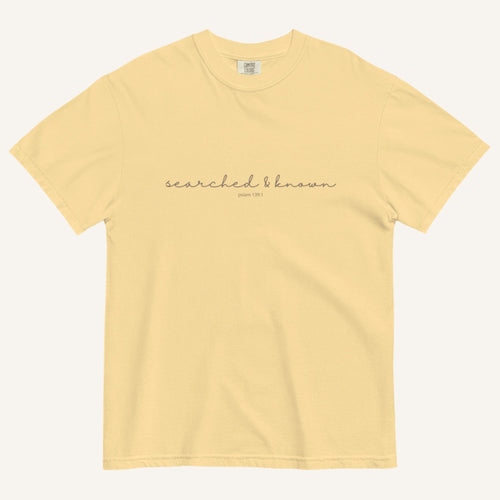yellow t-shirt with 'Searched & Known' text on a cream background