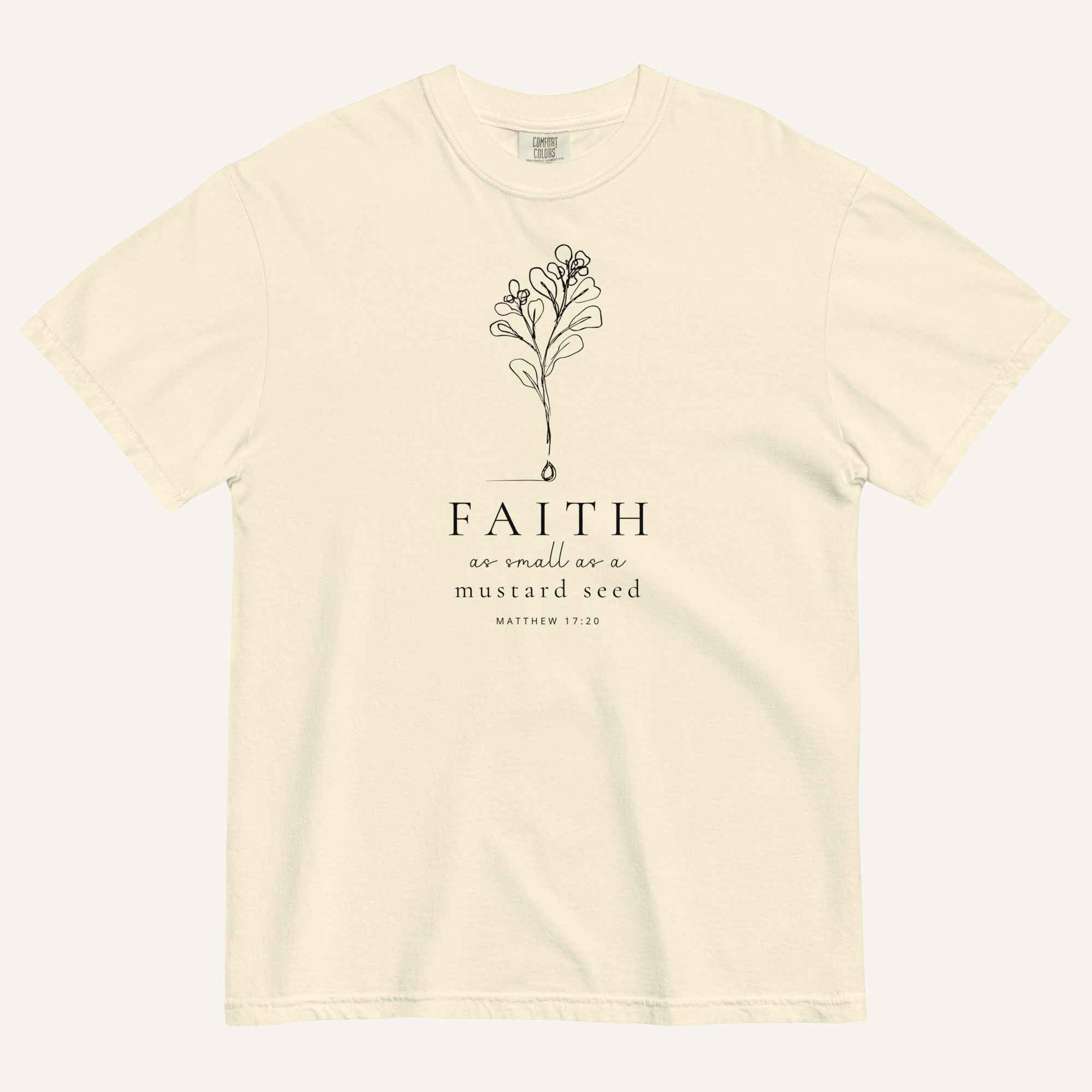 An ivory short-sleeve crewneck t-shirt with a black line-art mustard seed graphic and the text 'FAITH as small as a mustard seed' and 'MATTHEW 17:20' printed on the front, displayed against a light cream background.