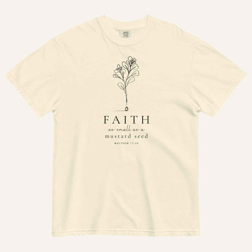 An ivory short-sleeve crewneck t-shirt with a black line-art mustard seed graphic and the text 'FAITH as small as a mustard seed' and 'MATTHEW 17:20' printed on the front, displayed against a light cream background.
