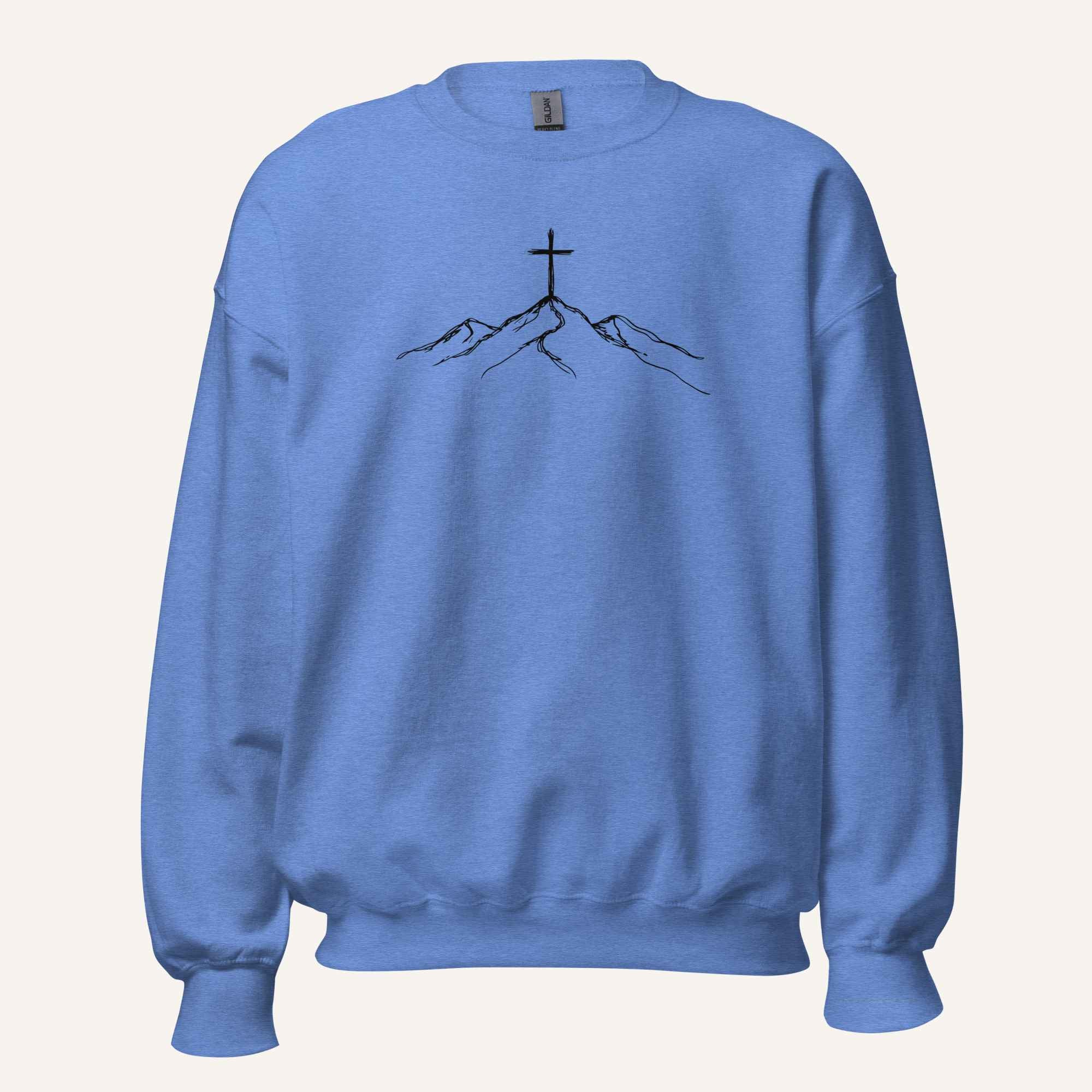 A blue crewneck sweatshirt featuring a black line art graphic of a cross on top of simple mountains on the chest, displayed against a solid off-white background.