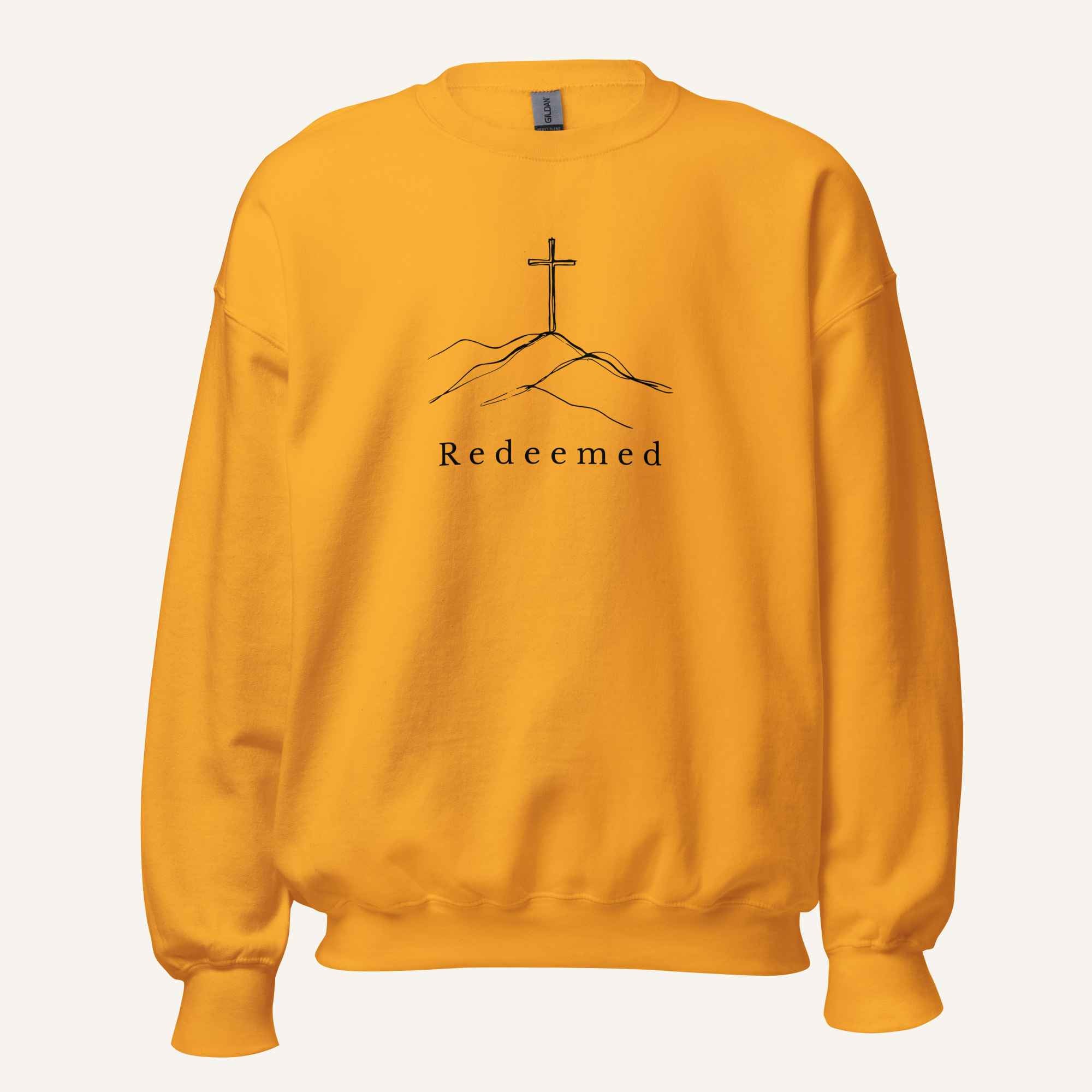 A yellow orange crewneck sweatshirt featuring a black graphic of a cross on a hill with the word 'Redeemed' printed below it, displayed on a clean off-white background.