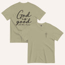 A light army green short-sleeve t-shirt shown from both the front and back on a light cream background. The back features the phrase 'God is good all the time' in black script, and the front has a small black cross on the left chest.