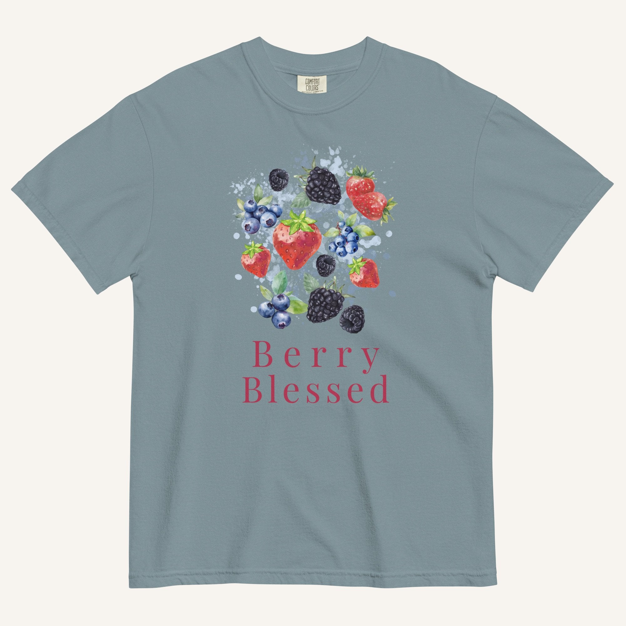 A slate blue crewneck t-shirt featuring a watercolor graphic of strawberries, blueberries, and blackberries with the text 'Berry Blessed' printed below in berry red, displayed on a light cream background.