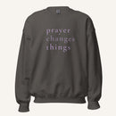 dark grey sweatshirt with 'Prayer Changes Things' purple text on a cream background