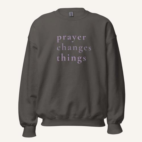 dark grey sweatshirt with 'Prayer Changes Things' purple text on a cream background